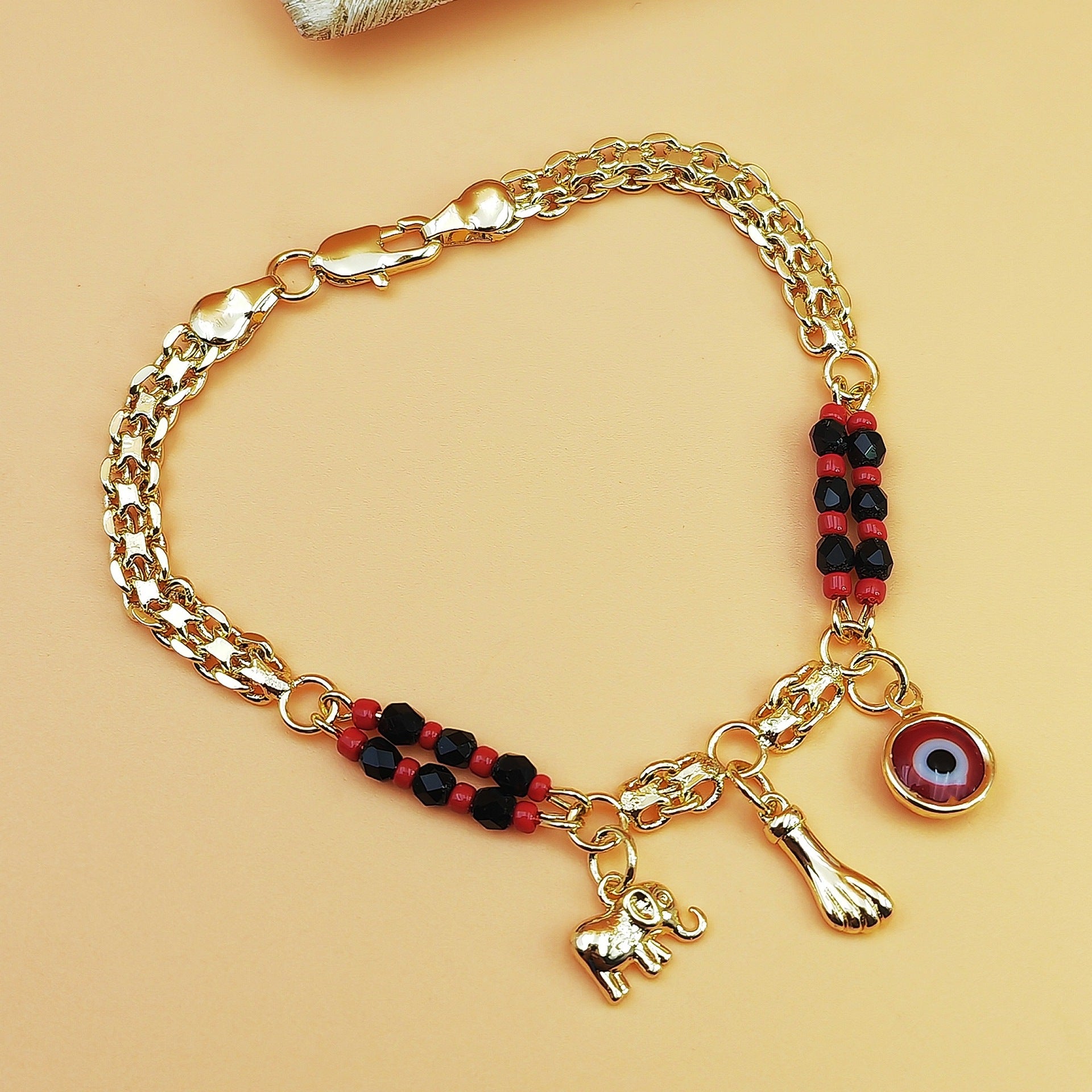 Gold-Tone Chain Bracelet with Red and Black Beads, Elephant Charm, Feather Pendant, and Round Stone Accent – 19 cm Length